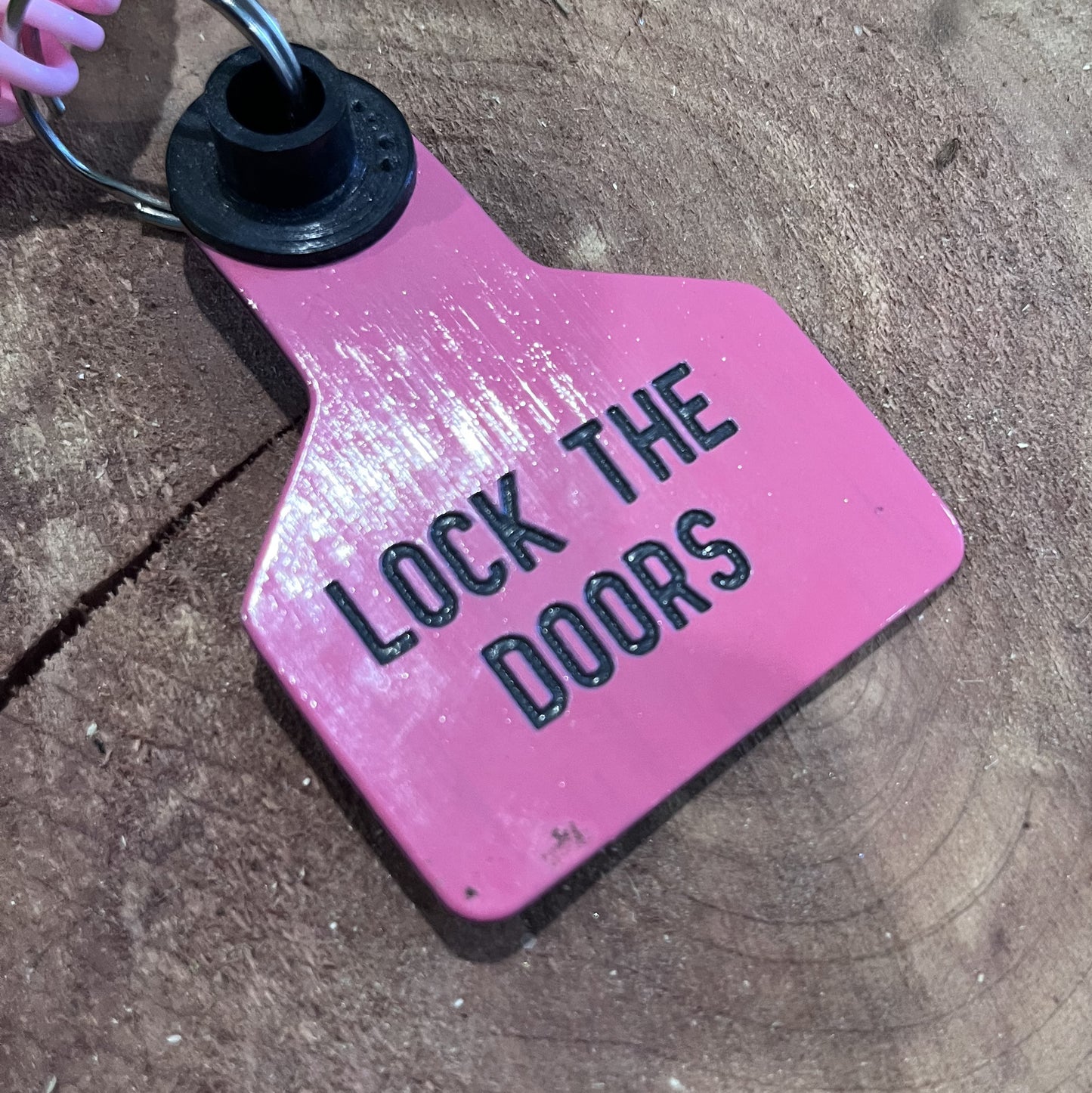 Pink keychain with 'LOCK THE DOORS' text on a concrete surface