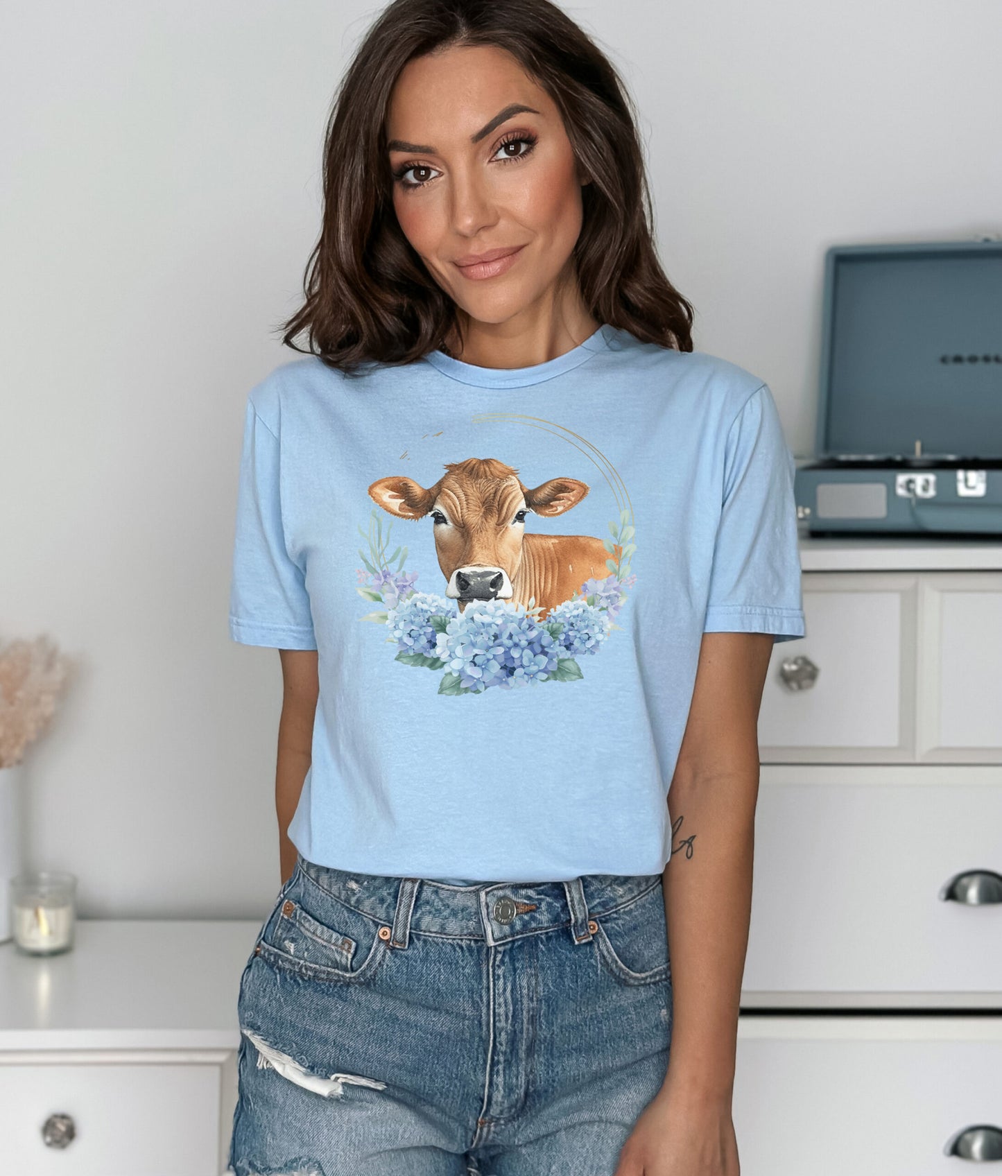 Woman wearing a light blue t-shirt with a cow and floral design in a kitchen.