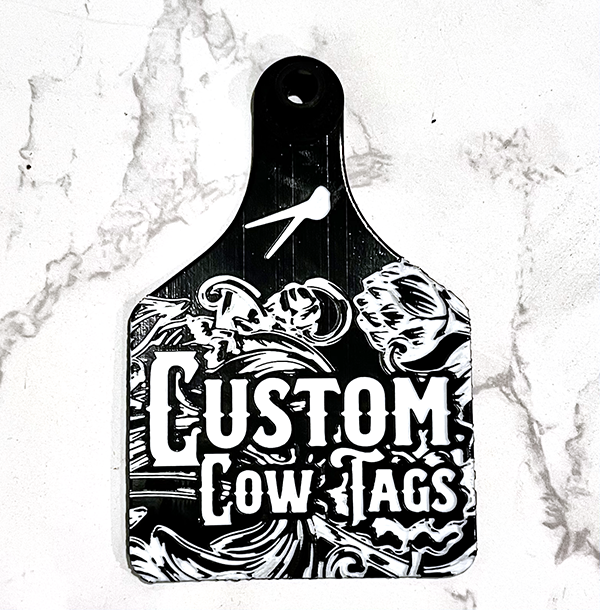Black cutting board with 'Custom Cow Tags' design on a marble background