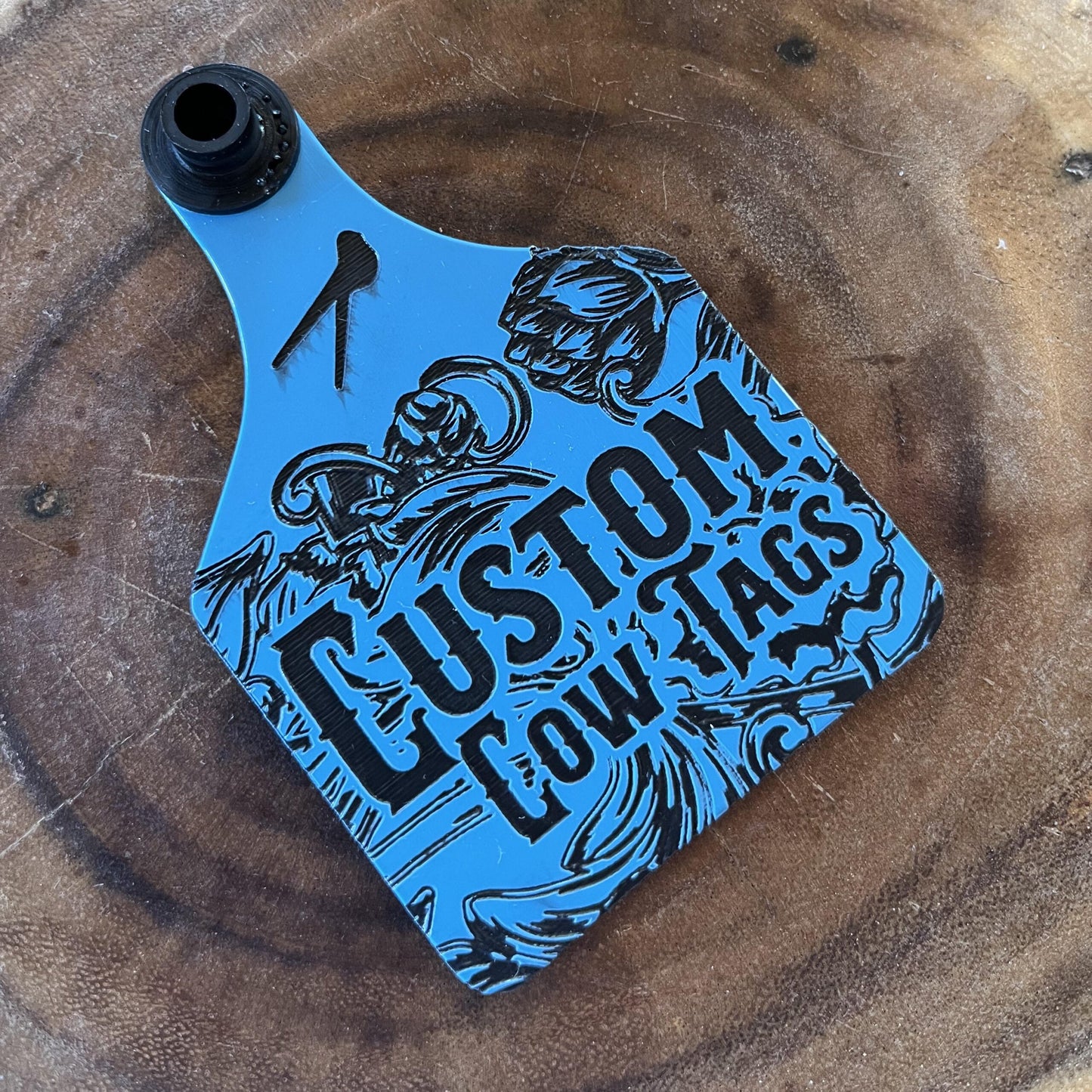 Blue and black 'Custom Cow Tags' product on a wooden surface