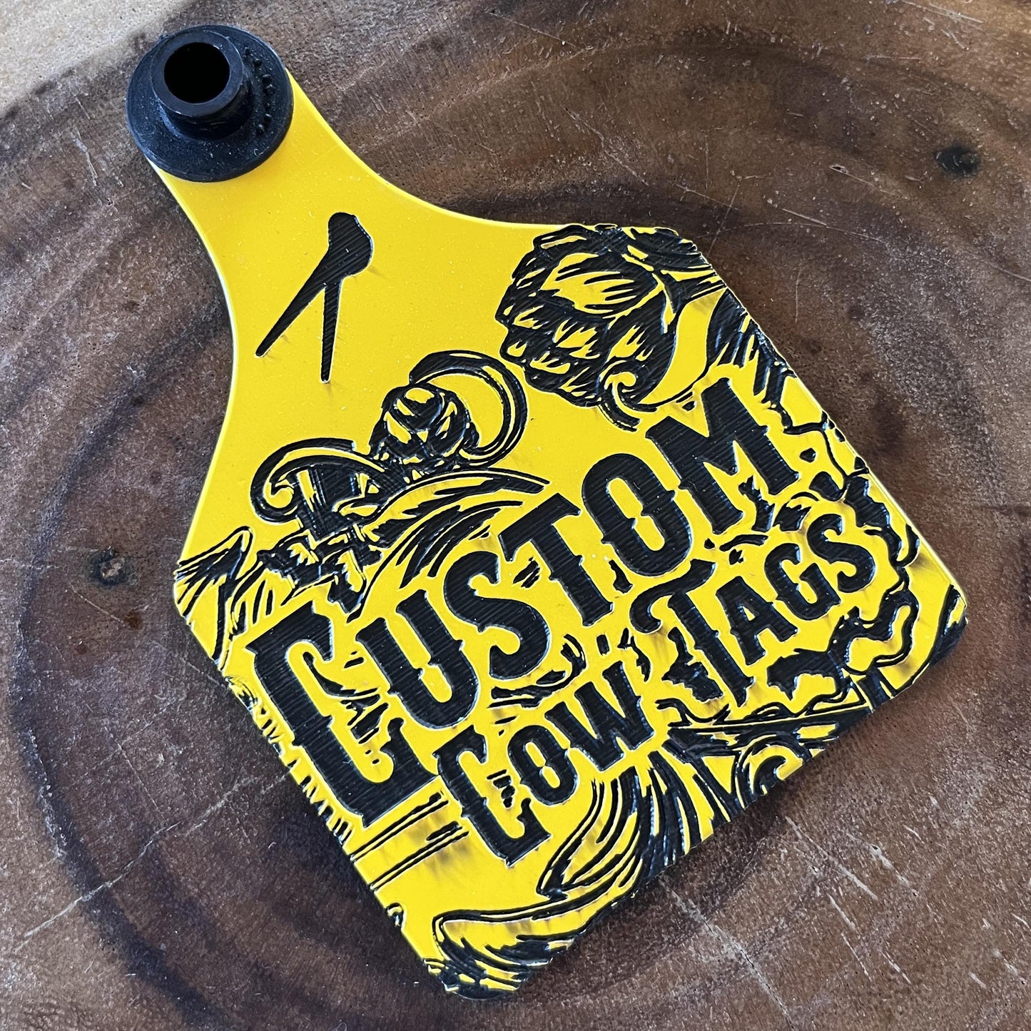 Yellow and black custom cow tag on a wooden surface