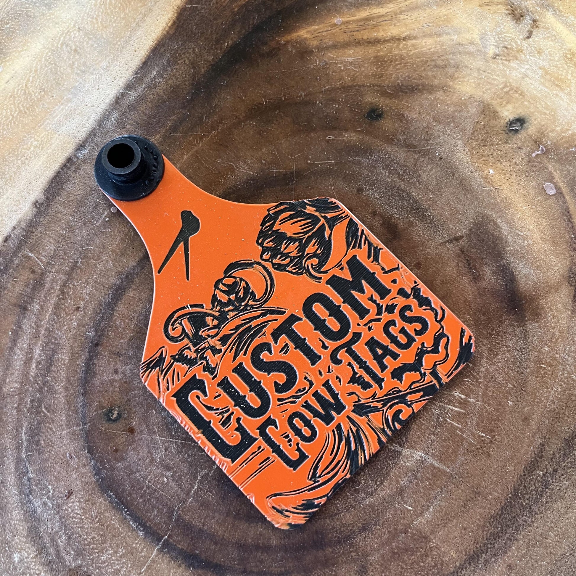 Orange and black 'Custom cow tags' decal on a wooden surface