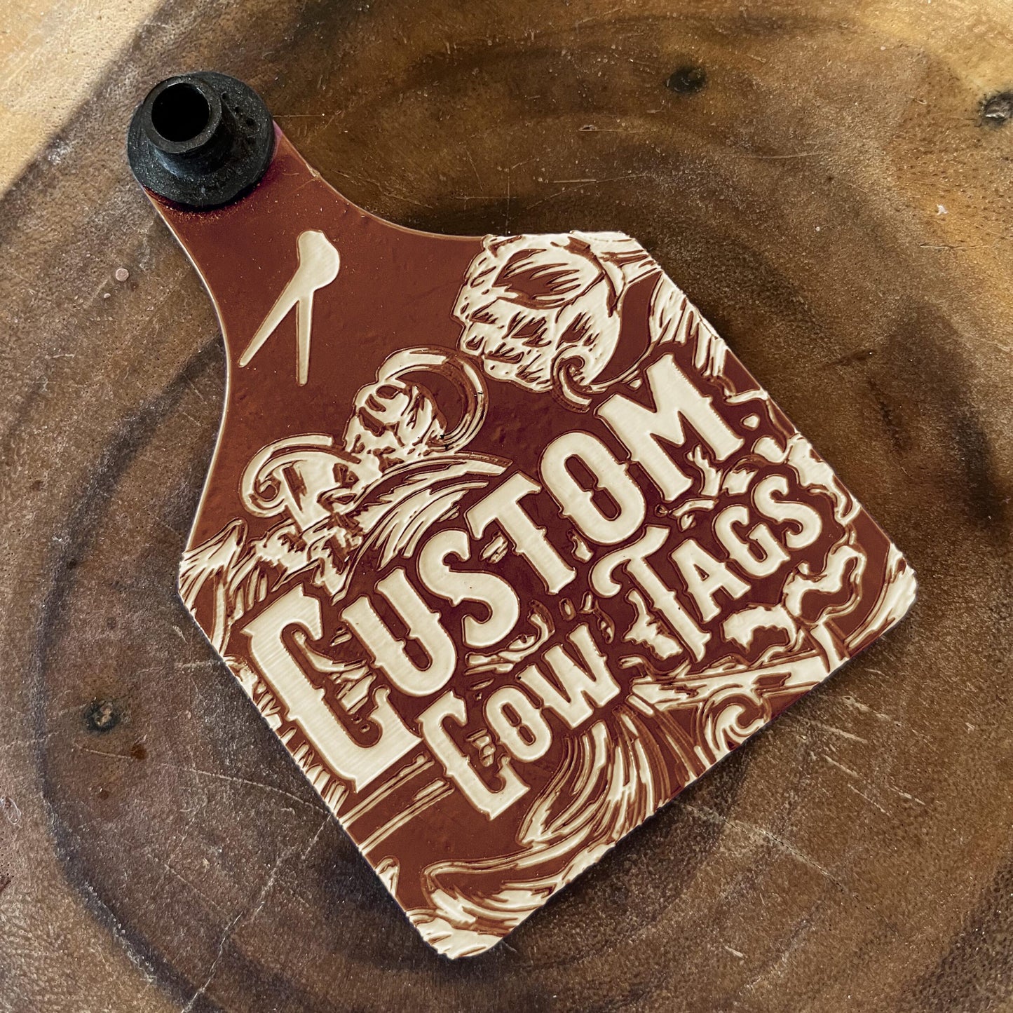 Custom cow tag with engraved design on a wooden surface