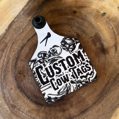 Custom cow tag with black and white design on a wooden surface