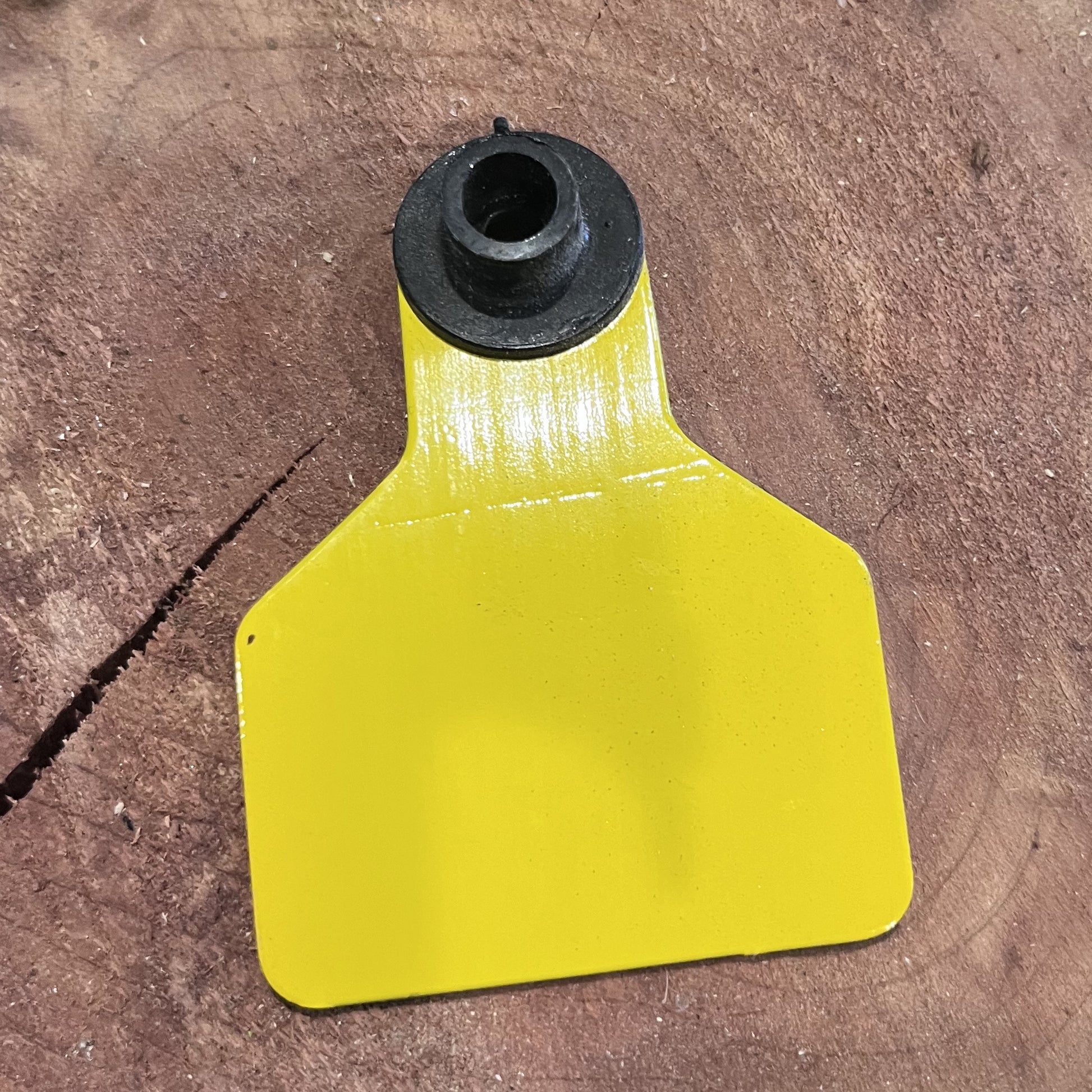 Yellow plastic tag with black rubber grommet on a brown surface
