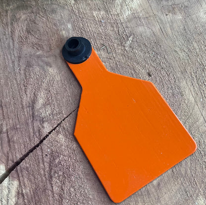 Orange plastic medium cow tag on a wooden surface with greenery in the corner