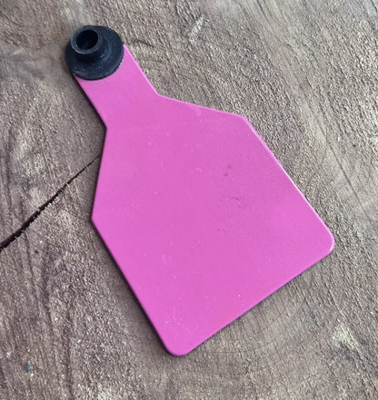 hot pink plastic medium cow tag on a wooden surface with greenery in the corner