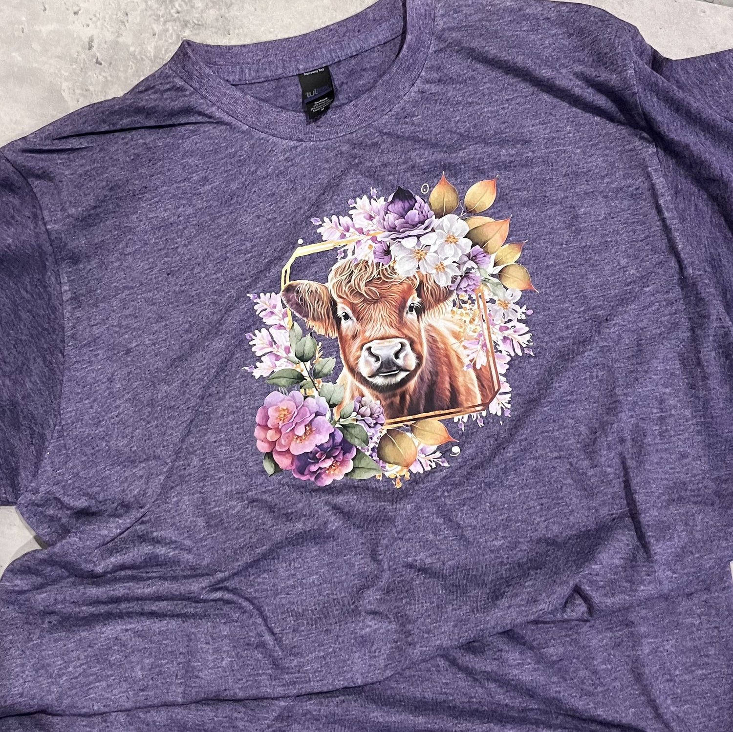 Purple tee shirt with a cow and floral design on a gray surface