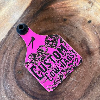 Pink and black 'Custom cow Tags' on a wooden surface