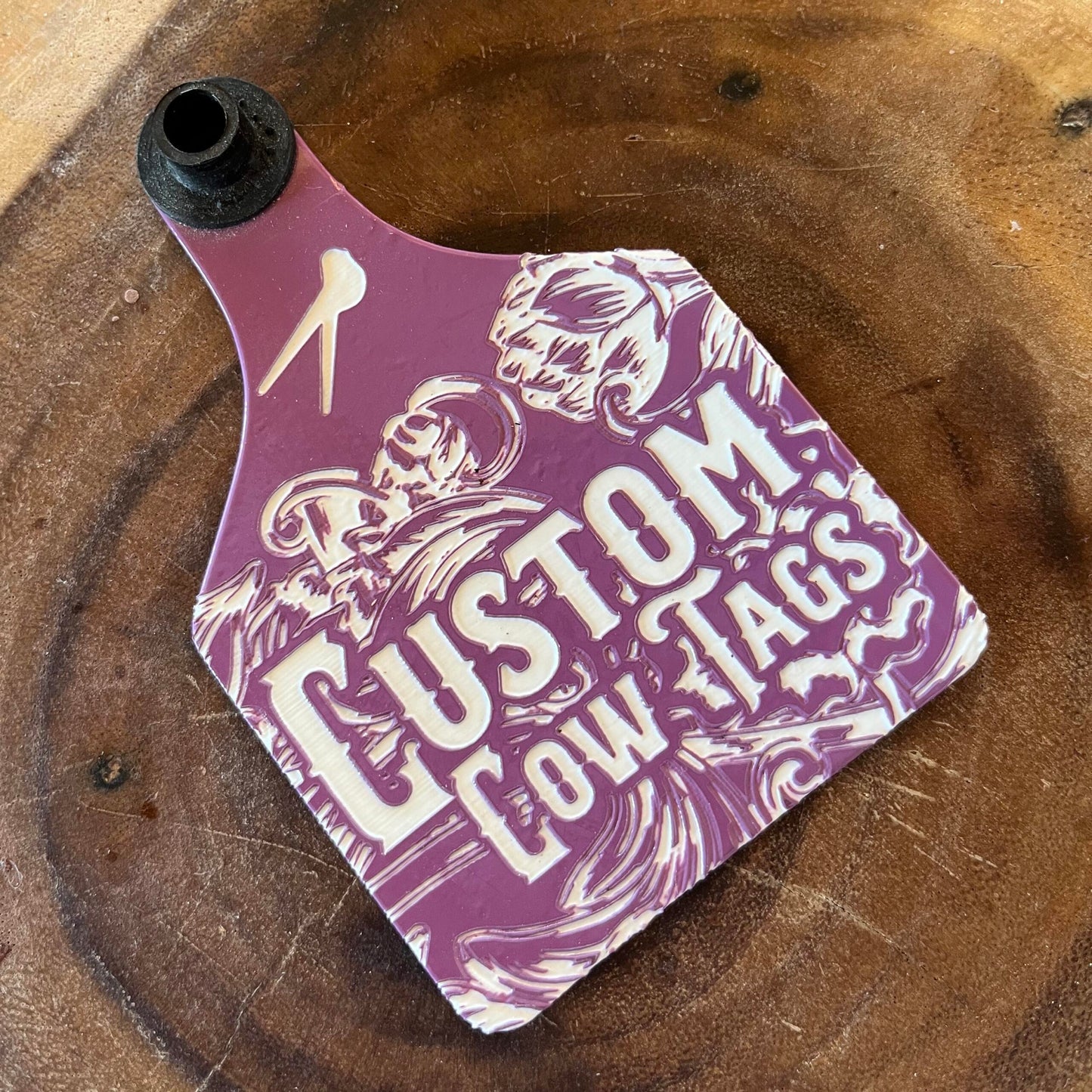 Purple custom cow tag with branding on a wooden surface