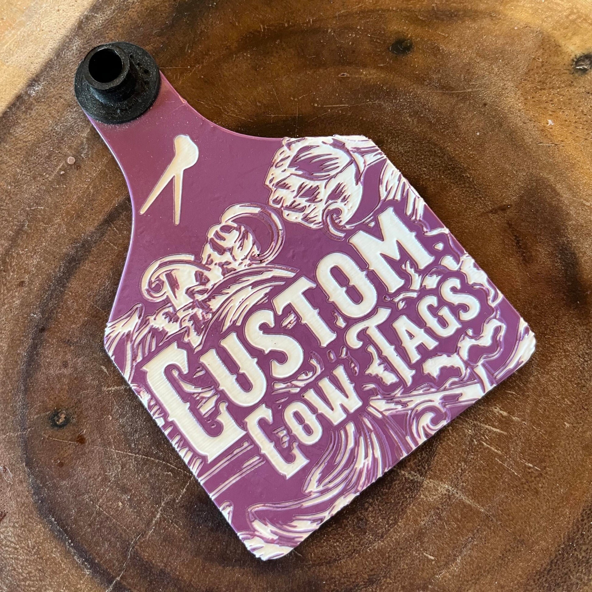 Purple custom cow tag with branding on a wooden surface