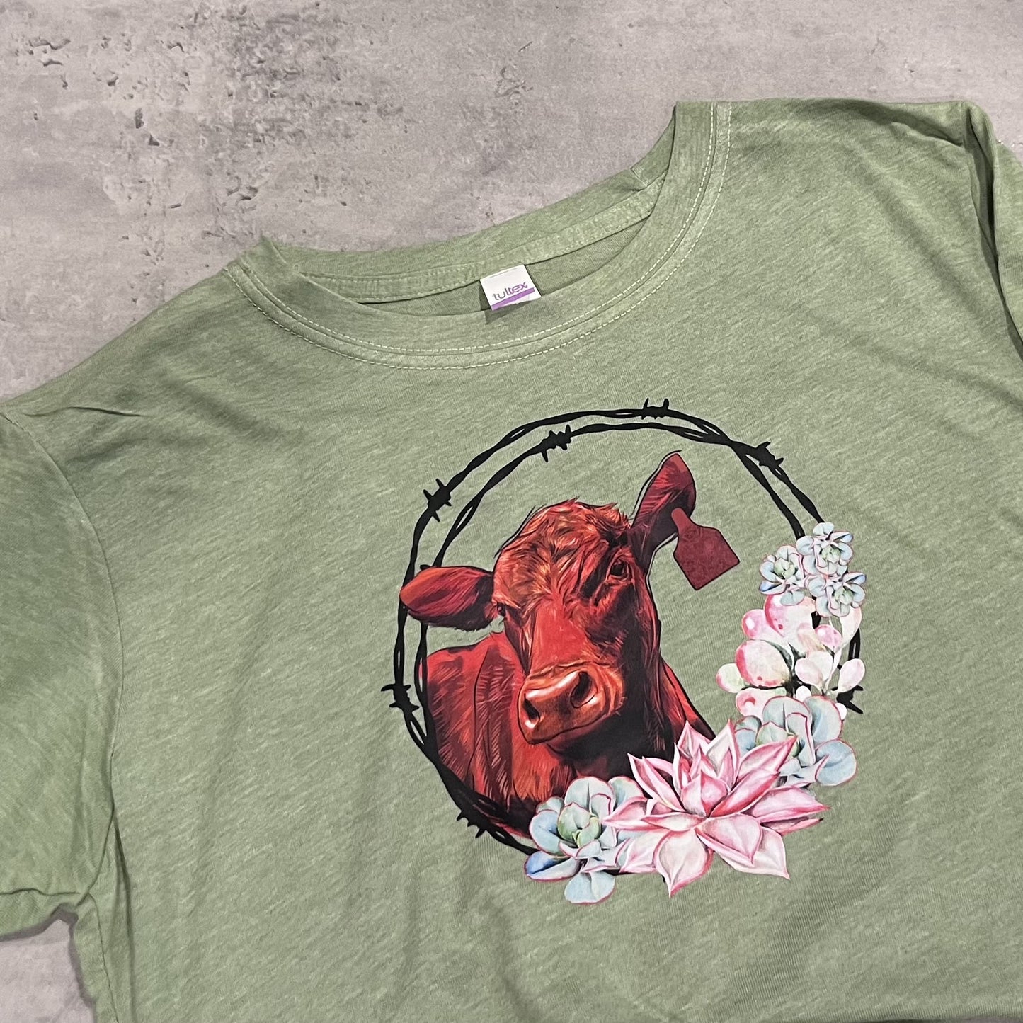 Green t-shirt with a red bull and floral design on a concrete surface